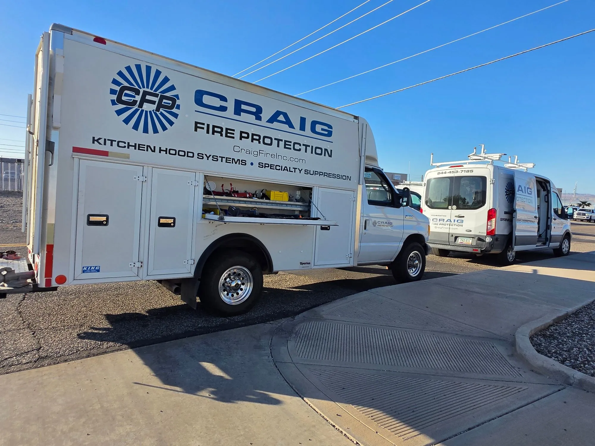 Craig Fire Protection service truck with its equipment compartments open, and a company van parked behind it