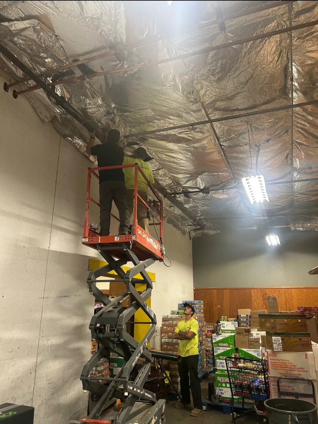 Craig Fire Protection technicians working on overhead piping from a scissor lift while a crew member watches from the floor