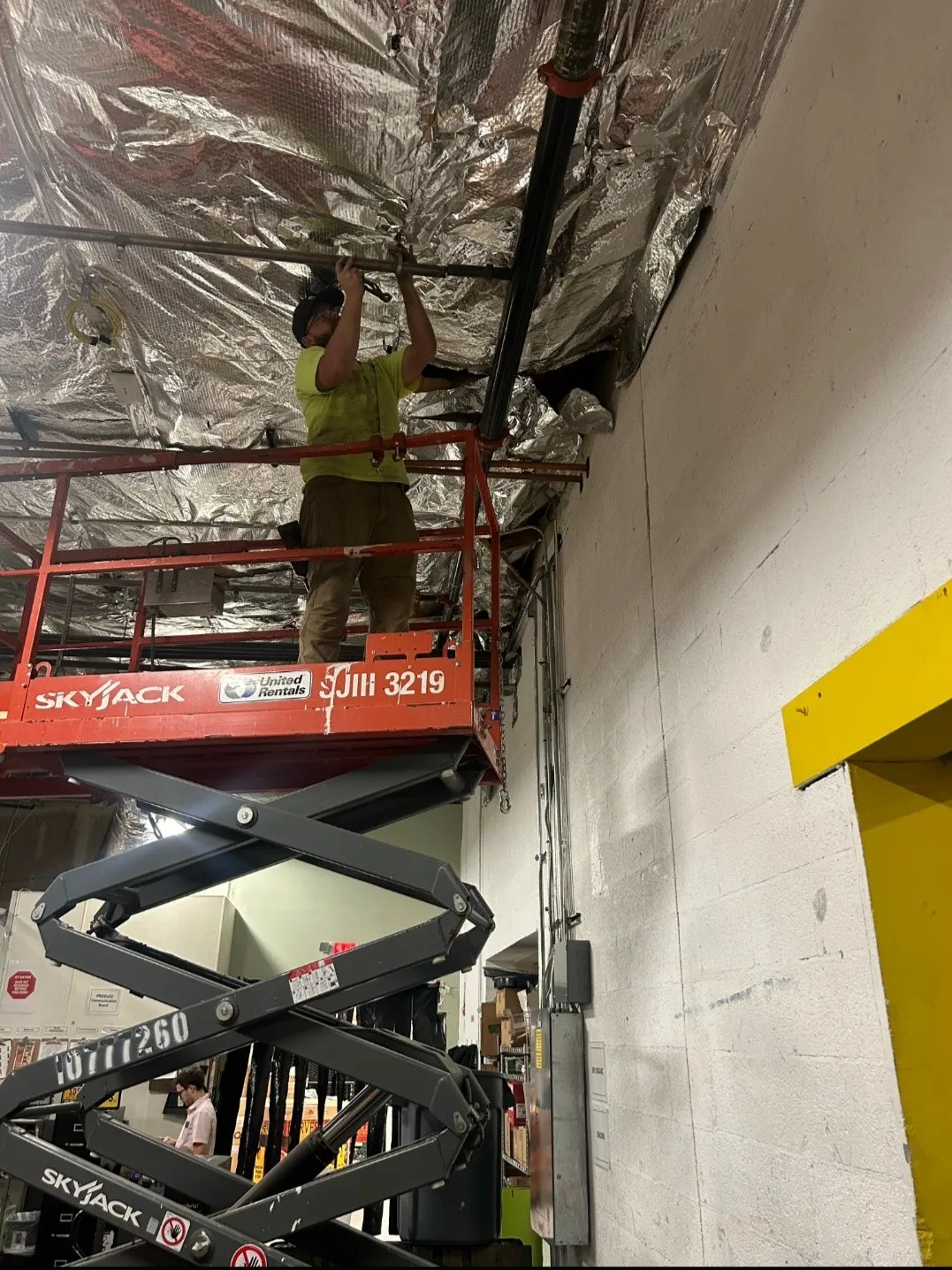 A Craig Fire Protection technician on a scissor lift working on overhead piping in a commercial stockroom