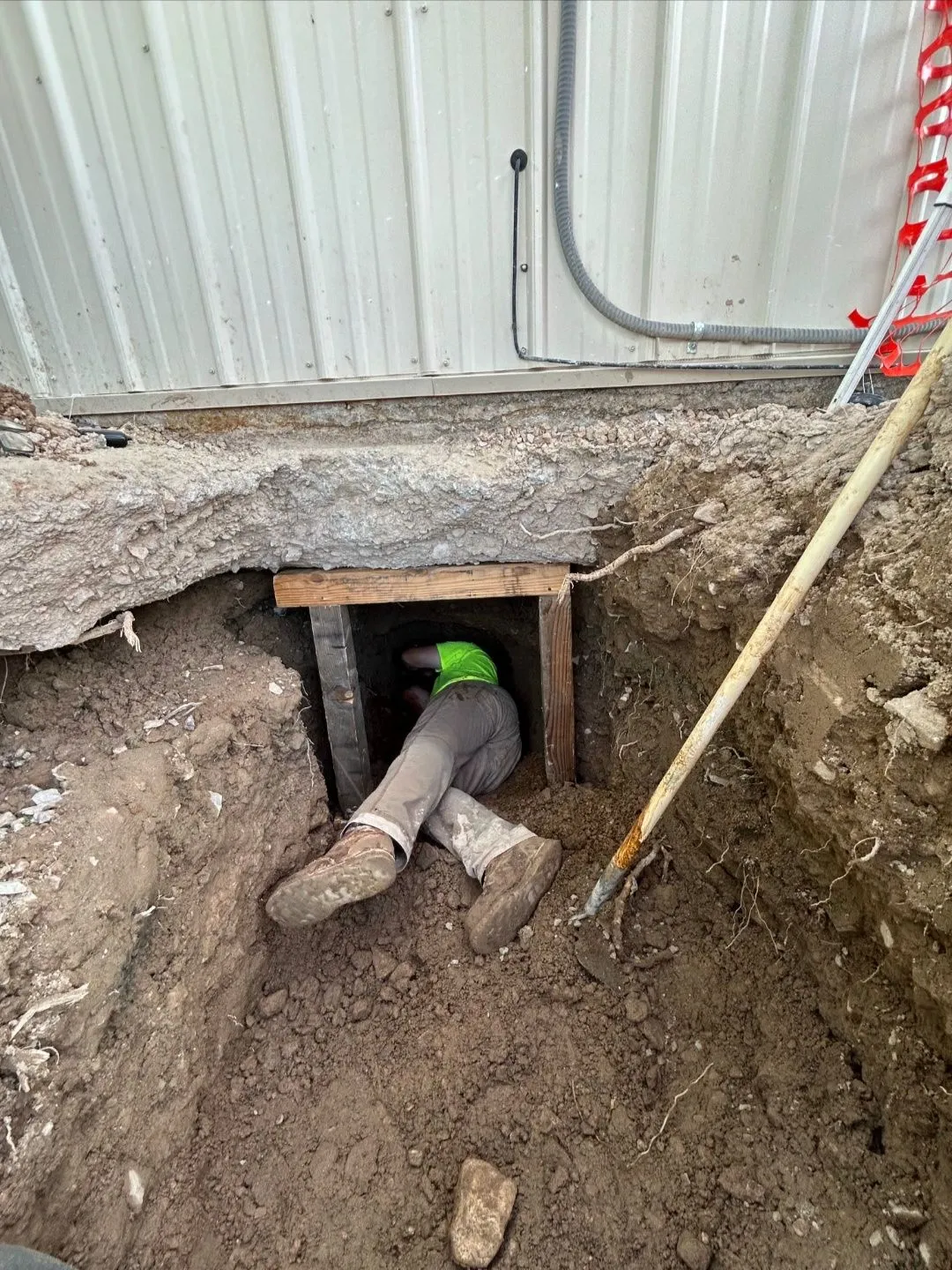 A Craig Fire Protection technician crawling through an excavated opening beneath a building's foundation